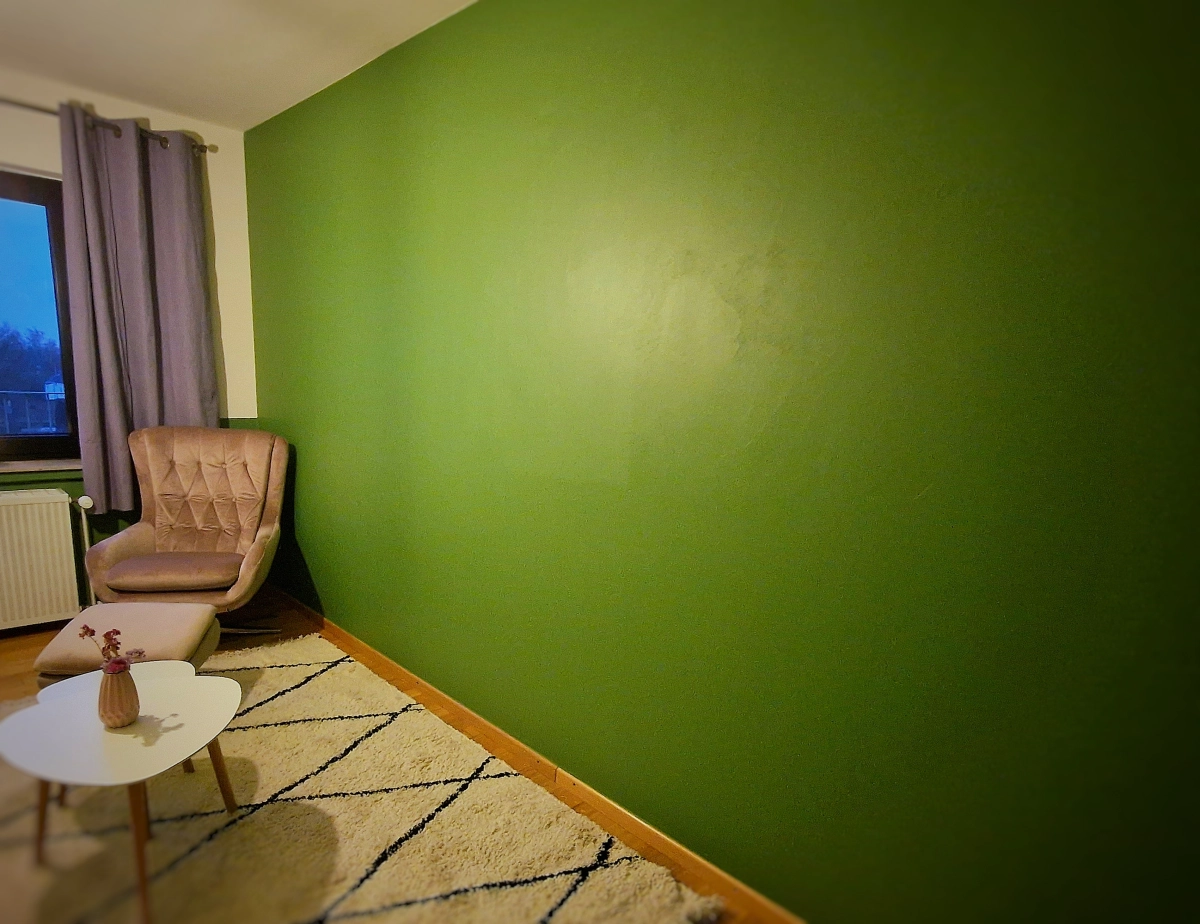 Wohnträume AS – André Santisi, grün bemalte Wand, Sessel und Couchtisch mit einer Blumenvase darauf
